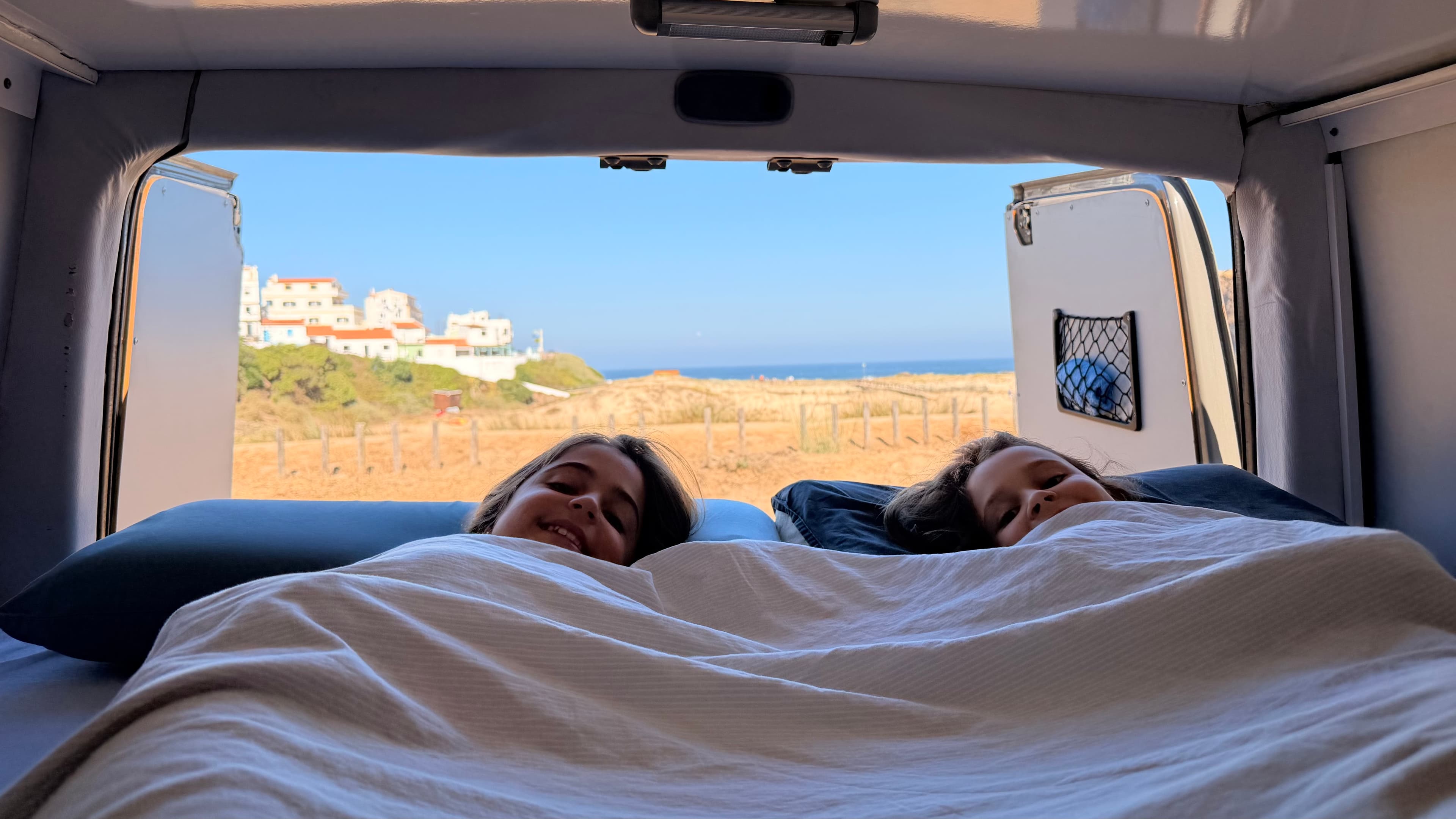 Las niñas asomando la cabeza en la cama, con vistas al pueblo y la playa de Odeceixe