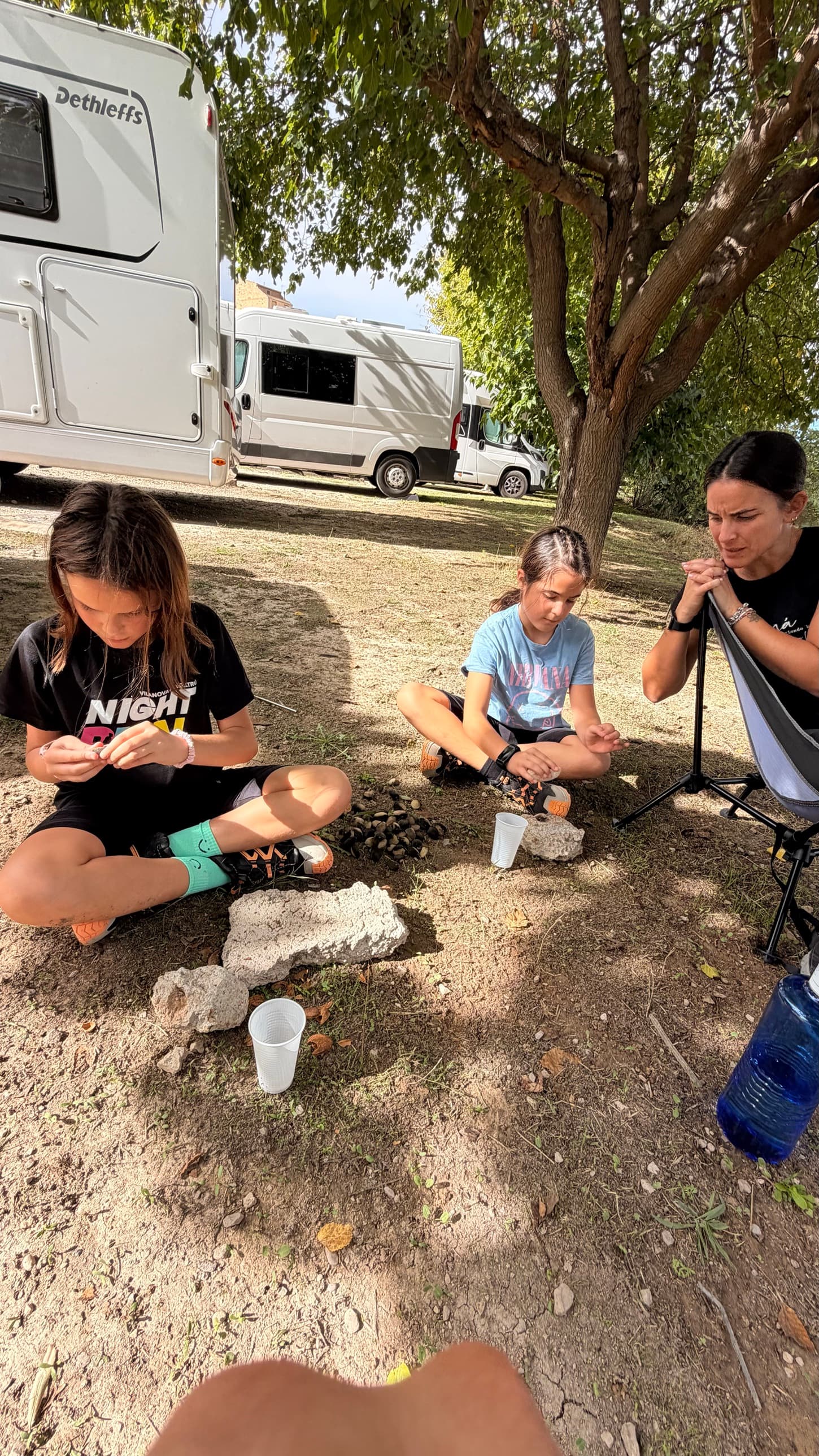 Niñas pelando almendras con piedras a la sombra en el área de autocaravanas de Horta de Sant Joan
